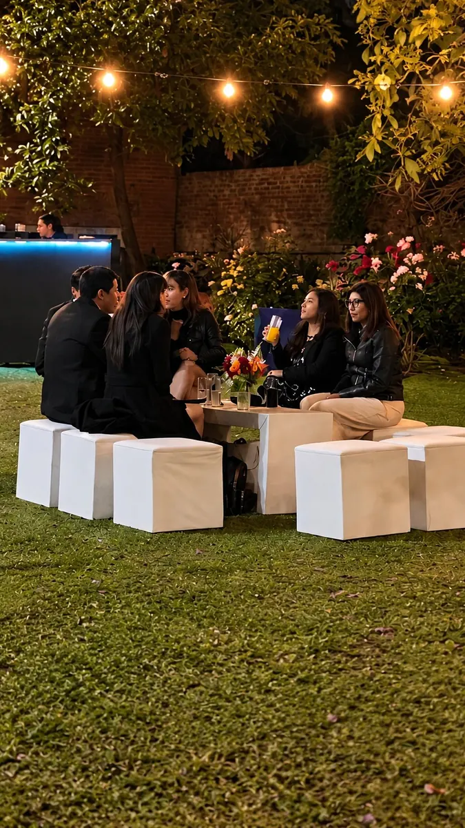 Grupo de invitados conversando de noche en el parque, sentados en puffs blancos